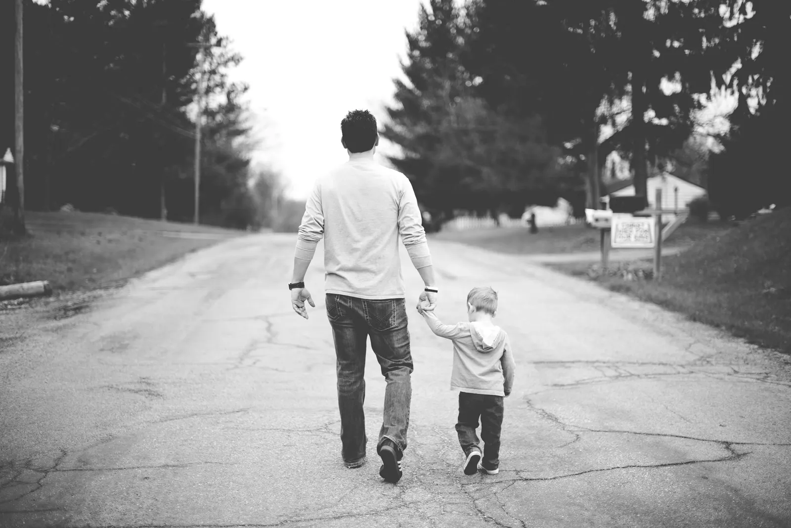 A dad and his young son walking hand in hand down a quiet road
